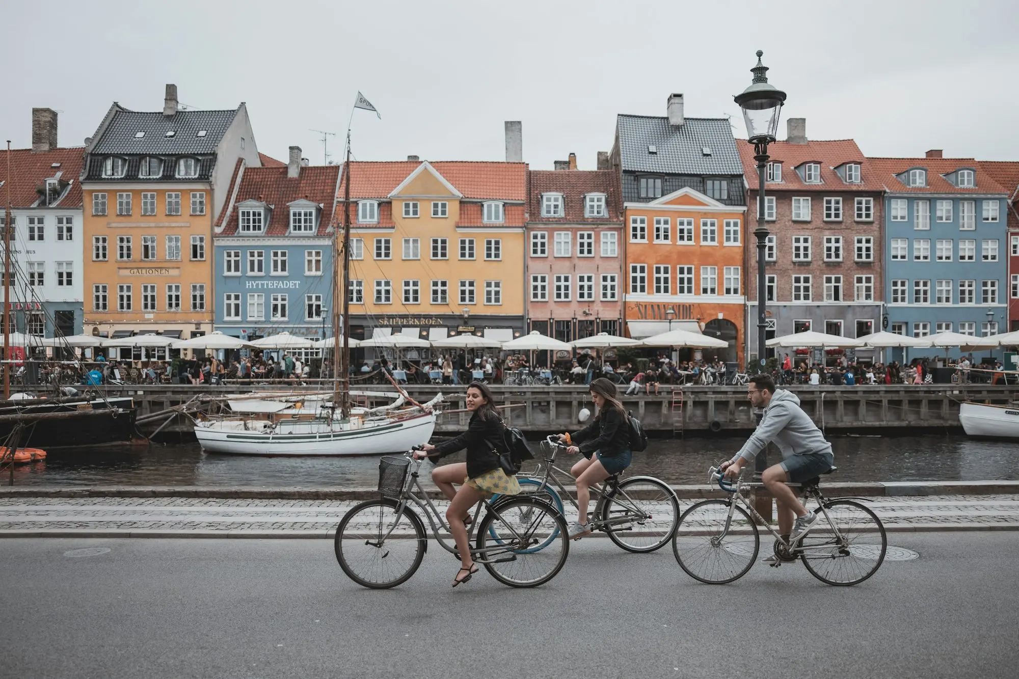Three people riding bicycles past the colorful houses of Nyhavn, Copenhagen