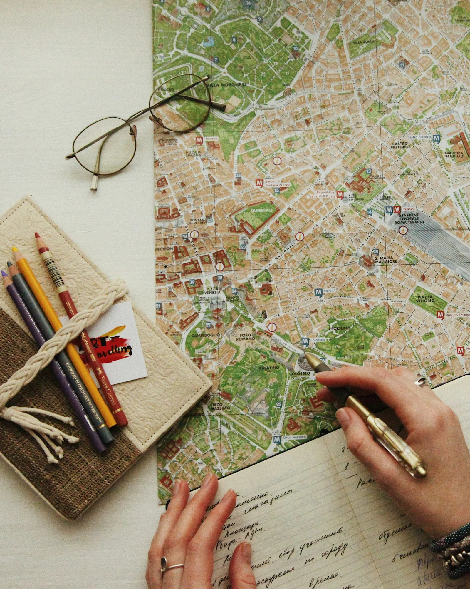 Hands marking a city map on a desk beside pencils and glasses